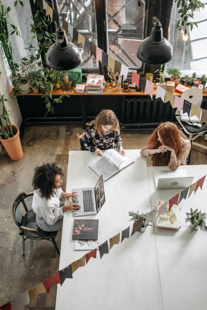 pexels-photo-6925381-6925381 Three women collaborate creatively in a cozy indoor workspace filled with plants.